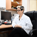 Dr Rita sits at her desk and smiles.